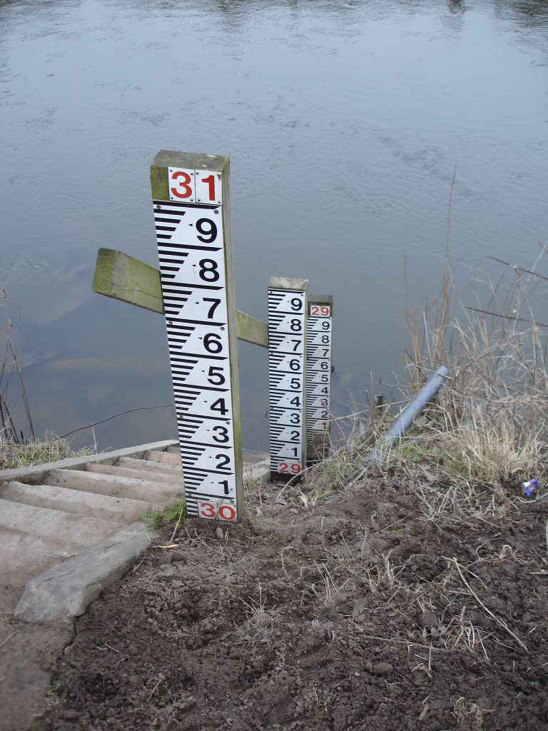A series of 1m long D50 gauge boards, each on an individual post and set at staggered heights down to the river