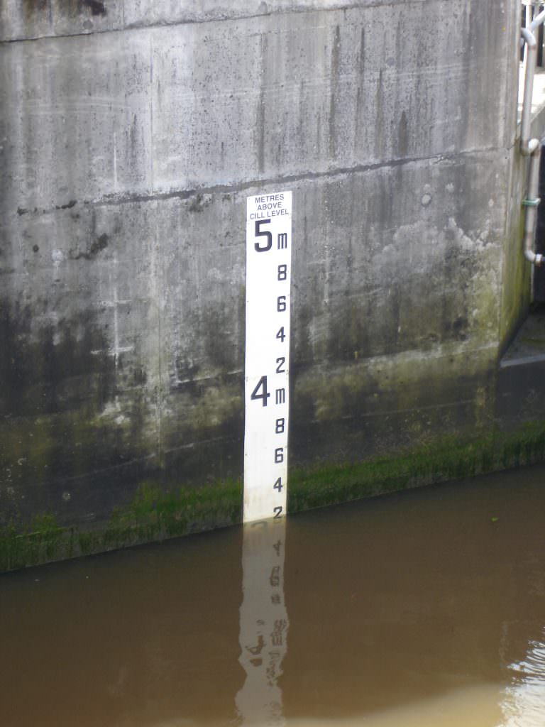 A D53 tidal gauge board with the metre graduations 4 & 5 visible above the tide height. Mounted on a concrete wall in Cardiff docks