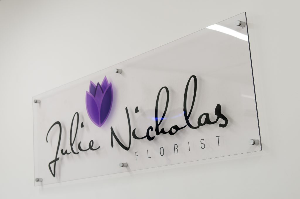 A clear acrylic shop sign located inside a florists.  Wall mounted but spaced off the wall giving the florist name & logo