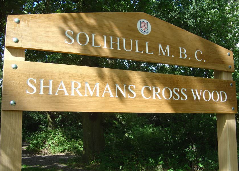 A routed oak park entrance sign with 2 planks. Mounted on oak posts. The text on both planks is indented and painted white.
