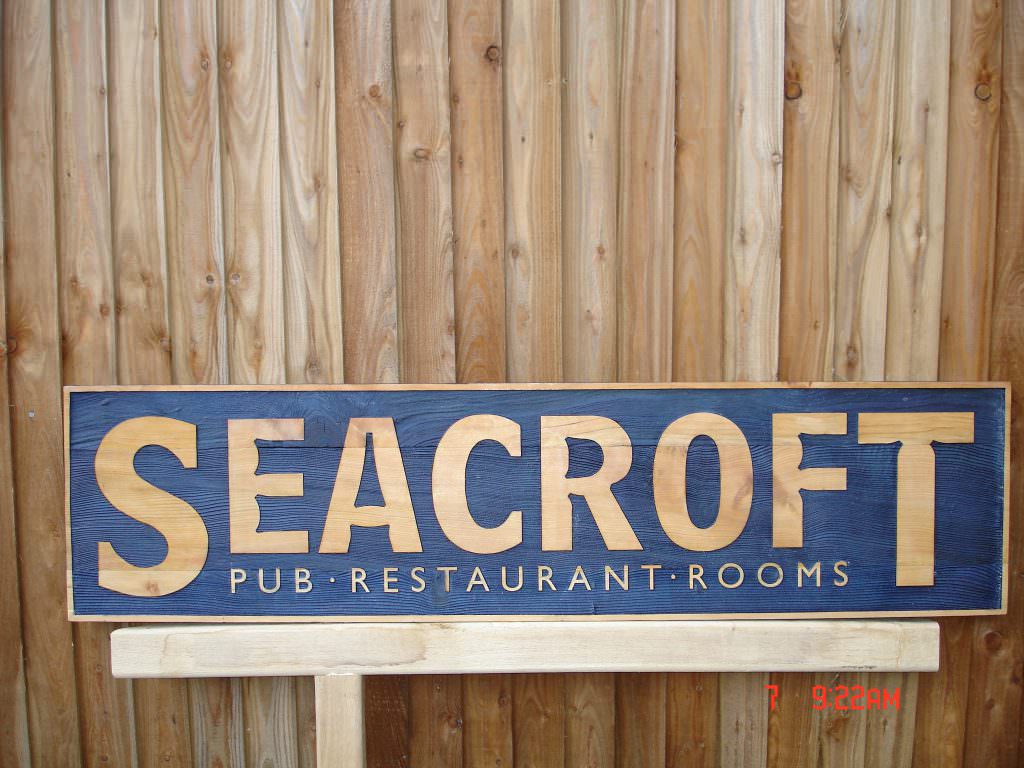 A sandblasted timber retail sign with tactile lettering and a dark blue background.  Wall mounted.